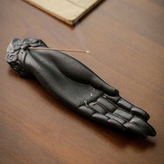 Buddha Hand Incense Burner – incense residue on palm, lit stick with open book nearby on warm wood, contemplative