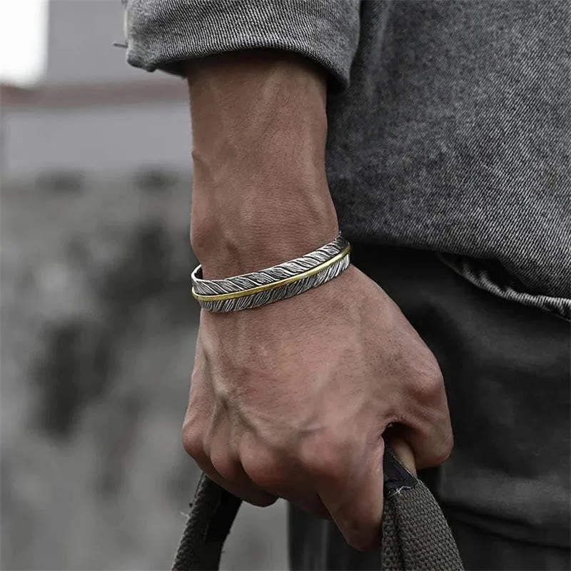 Two stacked feather cuff bracelets in silver and gold worn on man's wrist, bohemian mixed metal jewelry with urban street lifestyle styling
