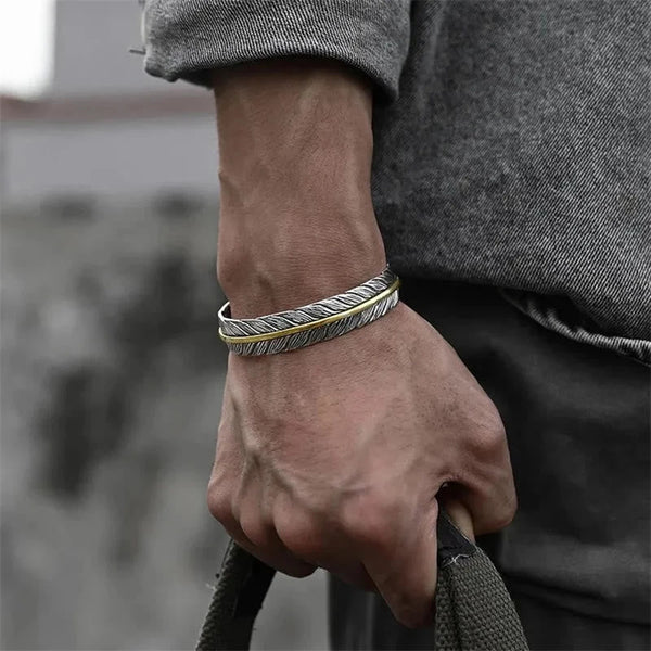Two stacked feather cuff bracelets in silver and gold worn on man's wrist, bohemian mixed metal jewelry with urban street lifestyle styling