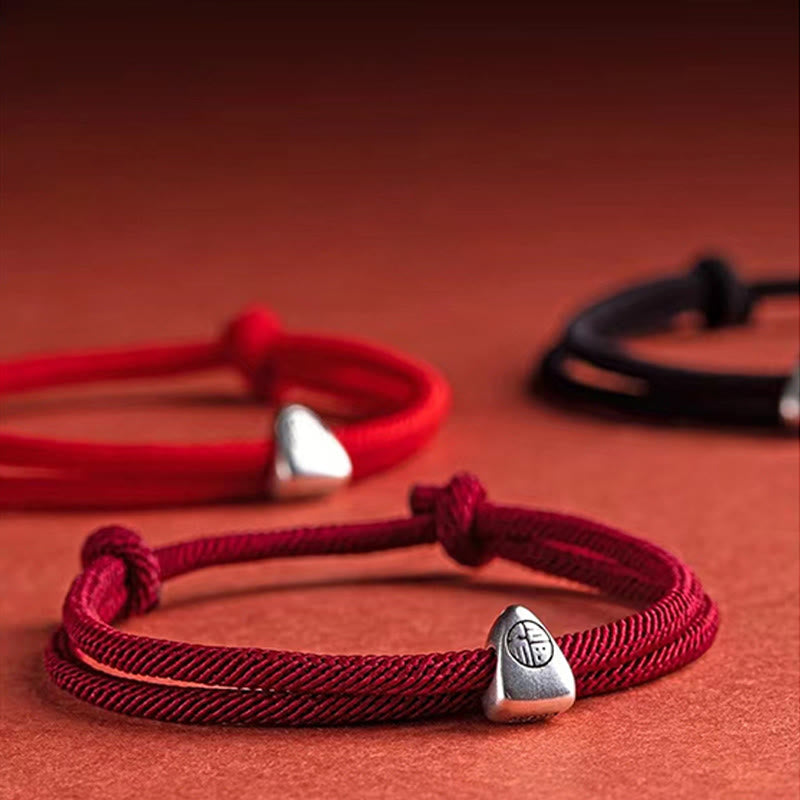 925 Silver Fu Character Braided Bracelet – Black braided cord with silver fortune charm and adjustable knot on terracotta red background, low angle product shot