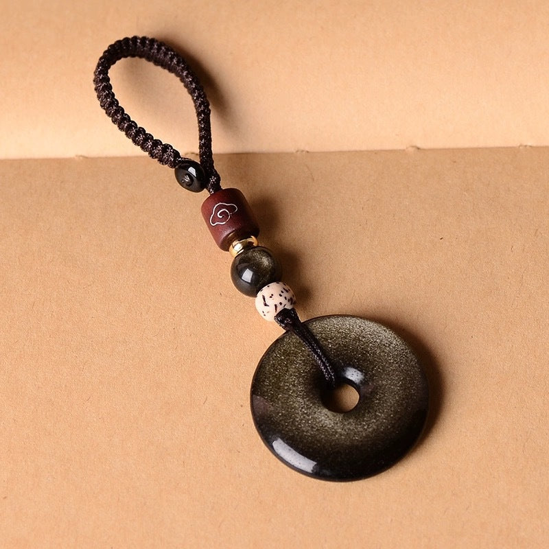 Gold Obsidian Pendant – Gold sheen obsidian keychain with brown cord loop on tan background, obsidian jewelry