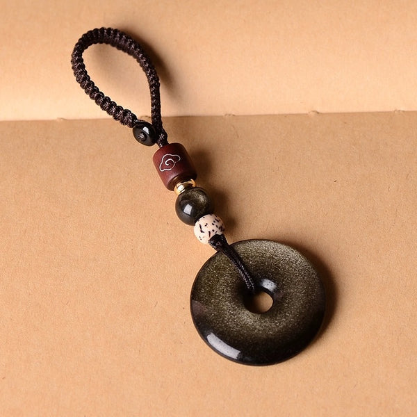 Gold Obsidian Pendant – Gold sheen obsidian keychain with brown cord loop on tan background, obsidian jewelry