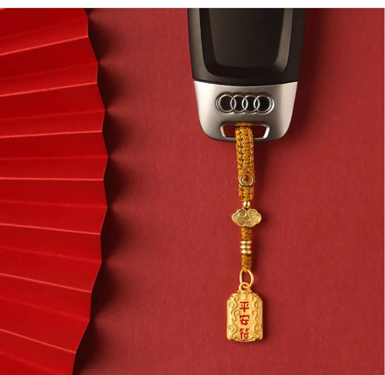 Brass peace charm keychain with gold braided rope attached to car key, red background Imagen principal del producto