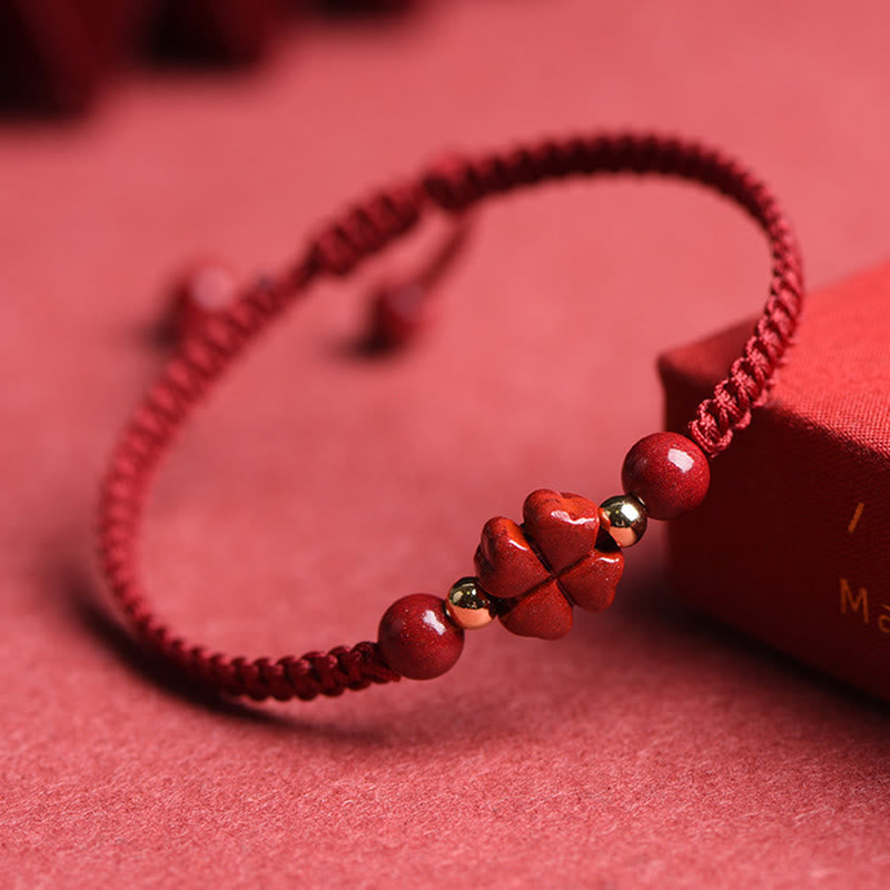 Adjustable burgundy macrame bracelet with carved red stone four-leaf clover centerpiece, gold spacer beads and round red beads on pink textured fabric