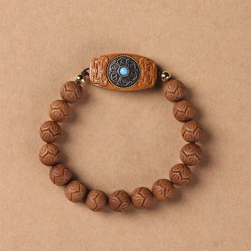 Green Sandalwood & Ebony Soothing Bracelet – direct overhead on warm tan surface, carved wood beads with eight-petal lotus...