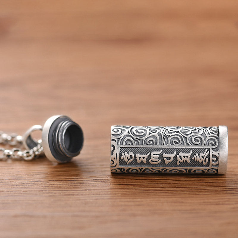 Om Mani Padme Hum Silver Protection Necklace – Opened silver cylindrical locket pendant revealing screw-top lid with Tibetan mantra inscription and spiral patterns on cable chain, displayed on wood surface