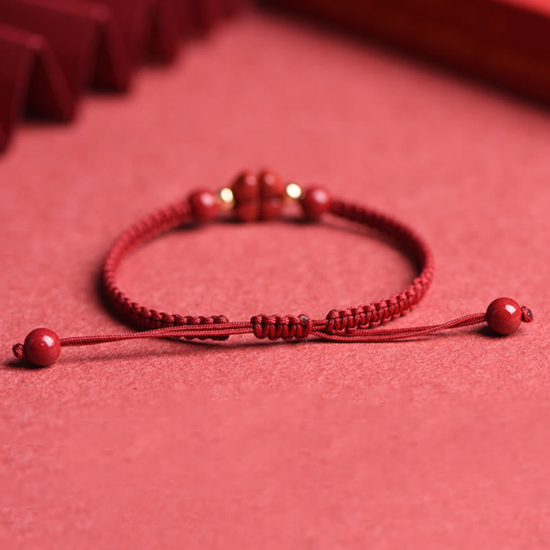 Red braided cord bracelet with carved cinnabar pig zodiac charm, gold accent beads and adjustable sliding knot closure on red background