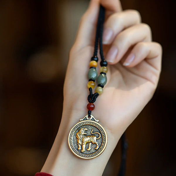 12 Chinese Zodiac Fortune Necklace Pendant – Tiger zodiac medallion pendant held in hand, antique gold brass with stippled background texture, roaring tiger relief, Greek key border, black cord with jade amber carnelian beads, traditional Chinese amulet necklace