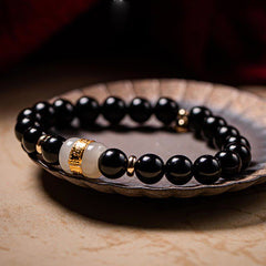 Black Obsidian Jade Bracelet – Low-angle macro in ceramic dish showing gold-banded jade center bead, beaded bracelet