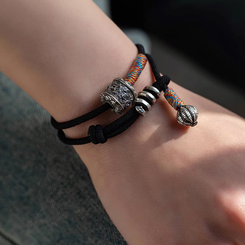 Tibetan Om Mani Padme Hum Wrap Bracelet – Hand-held showing double-wrap cord, silver engraved bead and colorful woven ends, beige background