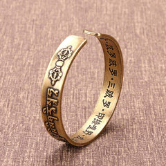 Brass open cuff bracelet with Vajra thunderbolt symbol, Tibetan mantra exterior and Chinese characters interior on brown woven fabric background