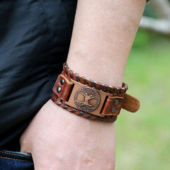 Tree of Life Copper Leather Bracelet – brown leather Tree of Life cuff worn on wrist, outdoor lifestyle photo with greenery