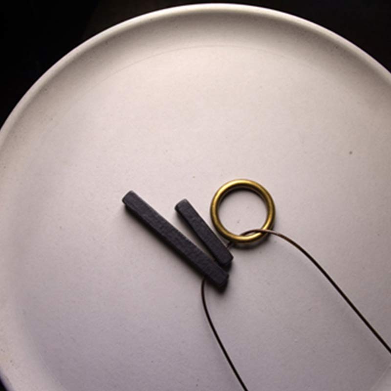 Zen Circle Ebony Wood Necklace - two dark bars with brass ring on off-white plate, flat lay photography