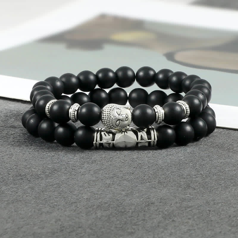 Natural Agate Buddha Protection Bracelet – Matte black Buddha bracelet on gray fabric with book background, lifestyle flatlay