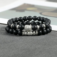 Natural Agate Buddha Protection Bracelet – Matte black Buddha bracelet on gray fabric with book background, lifestyle flatlay