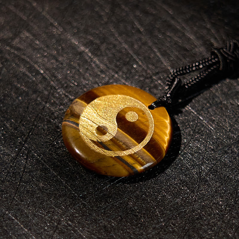 Yin Yang Crystal Necklace – Circular tiger eye stone pendant with gold yin-yang engraving on black cord, characteristic golde