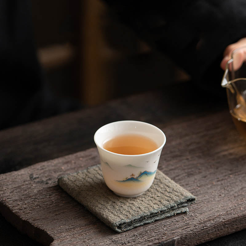 Ceramic Kung Fu Tea Cup – held in hand with amber tea, misty blue landscape visible, gongfu tea service, warm