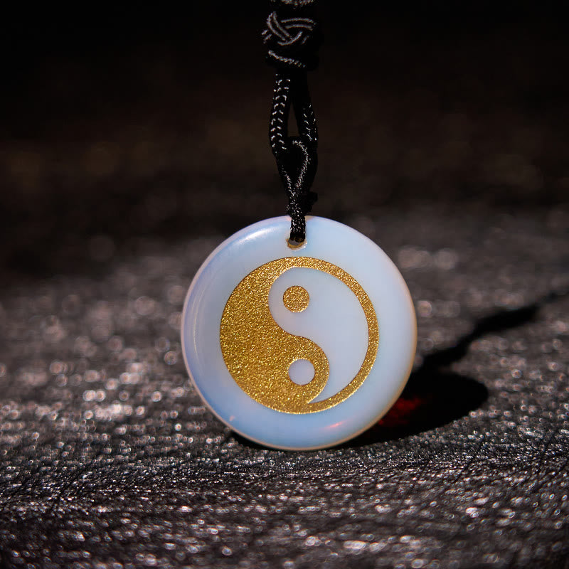 Yin Yang Crystal Necklace – Opalite stone pendant with gold yin-yang inlay, milky white opalescent disc with blue glow on bla