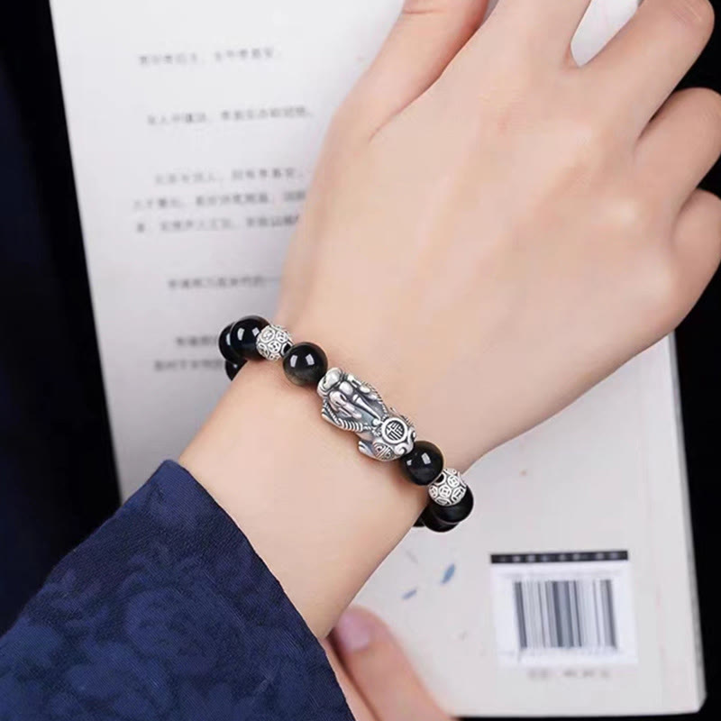 Gold Sheen Obsidian PiXiu Bracelet – Bracelet worn on wrist with blue sleeve over open book, protection jewelry