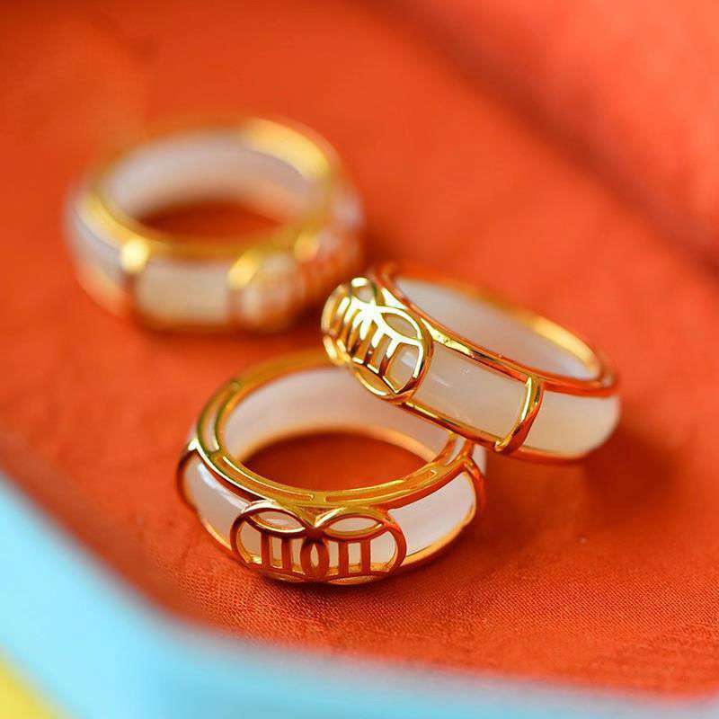 White Jade Luck Ring Necklace – Three white jade rings with gold filigree settings and traditional Chinese lattice patterns arranged on vibrant orange-red fabric