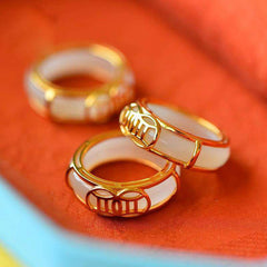 White Jade Luck Ring Necklace – Three white jade rings with gold filigree settings and traditional Chinese lattice patterns arranged on vibrant orange-red fabric