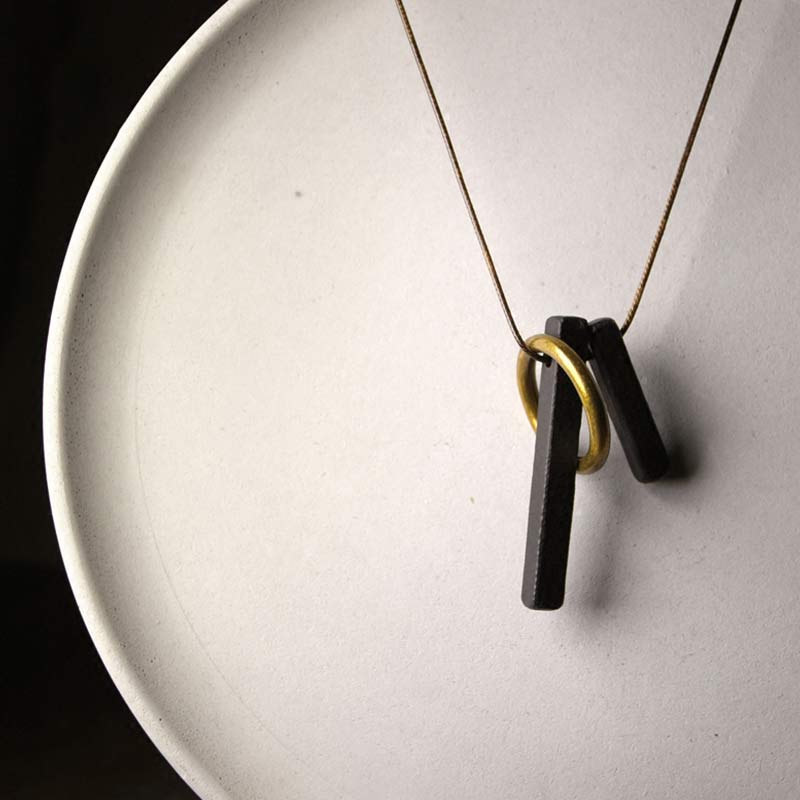 Zen Circle Ebony Wood Necklace - matte black bars with gold ring on gold chain, ceramic dish, warm lighting