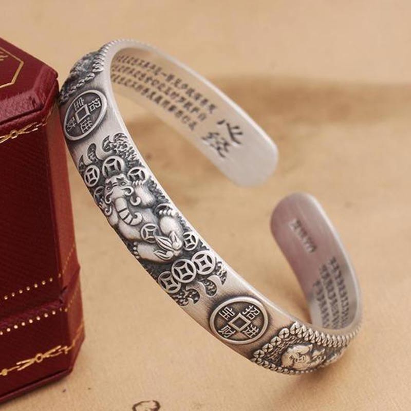 Silver feng shui Pixiu cuff bracelet with wealth beast carving, lucky coin medallions and Heart Sutra text, displayed with red gift box