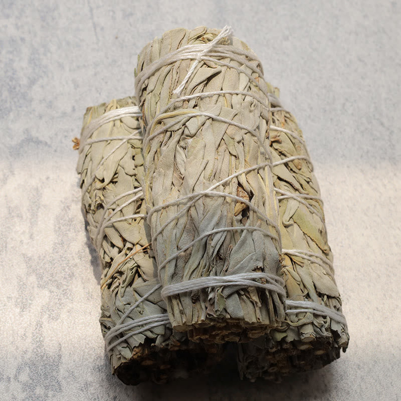 Three white sage smudge sticks stacked on gray stone, cleansing ritual