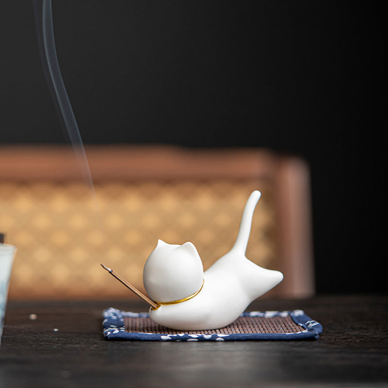 White ceramic cat incense holder with gold collar, smoke over dark wood surface
