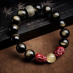 Gold Sheen Obsidian Pixiu Bracelet – diagonal on bamboo scroll and brown fabric showing golden flash obsidian beads, wealth luck