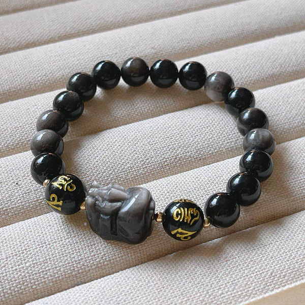 Om Mani Padme Hum Bracelet – Silver sheen obsidian beads with PiXiu on cream fabric display, meditation bracelet