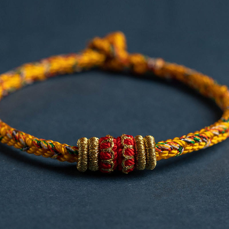 Handmade golden braided rope bracelet with gold and red cylindrical beads, adjustable sliding knot closure, traditional Chinese lucky knot jewelry on navy background