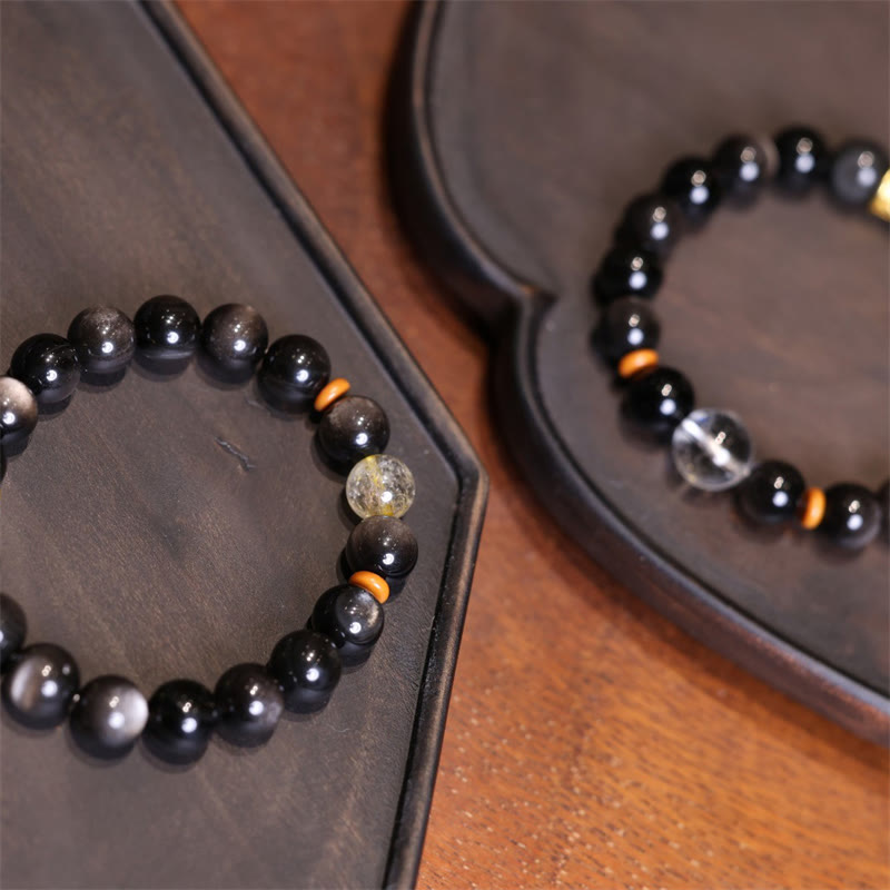 Silver Sheen Obsidian Mantra Bracelet – two bracelets on dark wood trays showing stone variations, men’s gemstone
