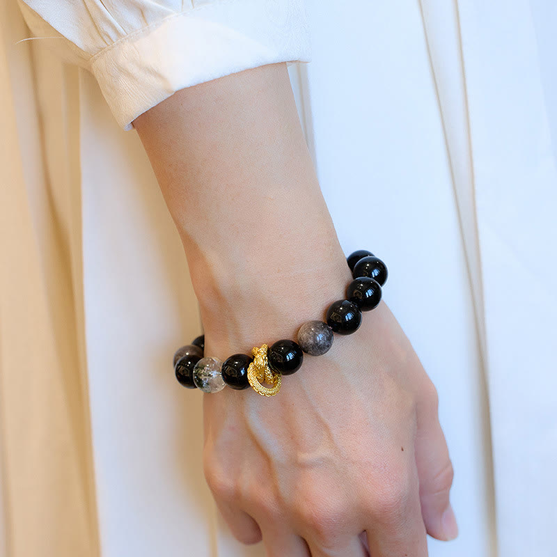 Silver Sheen Obsidian Dragon Bracelet – Worn on wrist over cream blouse, glossy black beads flanking gold dragon, empowering