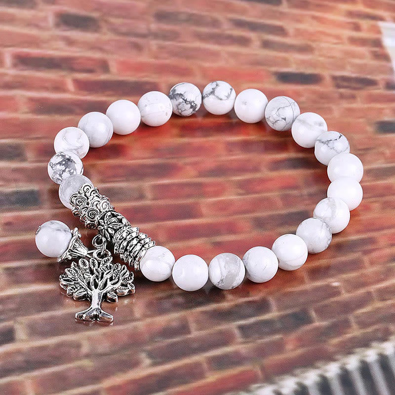 Tree of Life white turquoise bracelet with white and gray marbled beads, ornate silver cylindrical spacer, tree of life charm on brick background.
