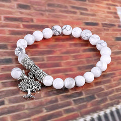 Tree of Life white turquoise bracelet with white and gray marbled beads, ornate silver cylindrical spacer, tree of life charm on brick background.