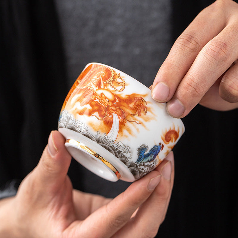 Dragon Phoenix Crane Gilt Ceramic Teacup – hand-painted dragon tea cup with gold interior held in hands, three-quarter view, artisan