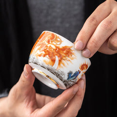 Dragon Phoenix Crane Gilt Ceramic Teacup – hand-painted dragon tea cup with gold interior held in hands, three-quarter view, artisan