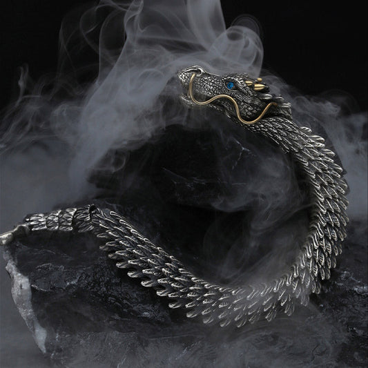 Dragon cuff bracelet with articulated scale segments blue gemstone eye gold whiskers and antiqued silver finish displayed in dynamic S-curve on dark stone with mist effects