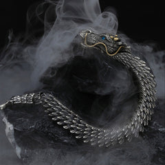 Dragon cuff bracelet with articulated scale segments blue gemstone eye gold whiskers and antiqued silver finish displayed in dynamic S-curve on dark stone with mist effects