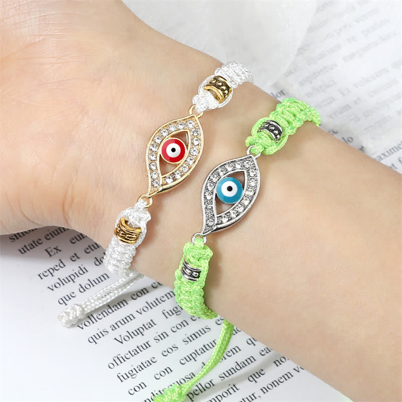 White and lime green cord evil eye bracelets stacked on wrist over open book