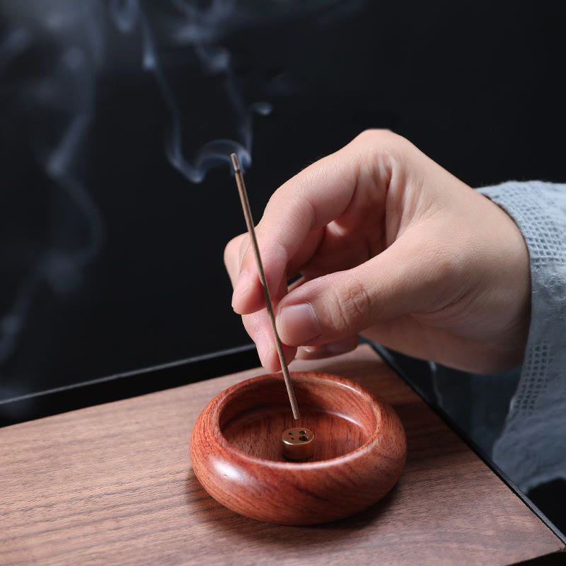 Rosewood incense bowl with burning stick and smoke on dark wood, mindful