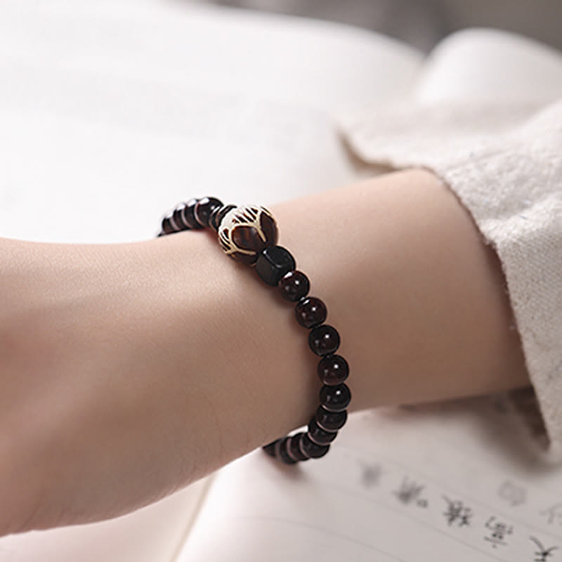 Red Sandalwood Lotus Bodhi Seed Bracelet – Burgundy beads with gold lotus filigree center worn on wrist, warm bokeh