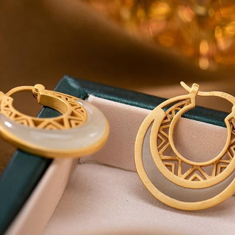 Crescent Moon Jade Drop Earrings – Gold double-ring hoops with white jade crescent and lattice cutouts on teal-tan velvet, lifestyle shallow depth, three-quarter