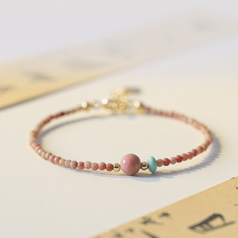 Rhodonite Loving Energy Bracelet – Pink to cream gradient stone beads with turquoise accent and gold spacers on white ceramic edge, low close-up