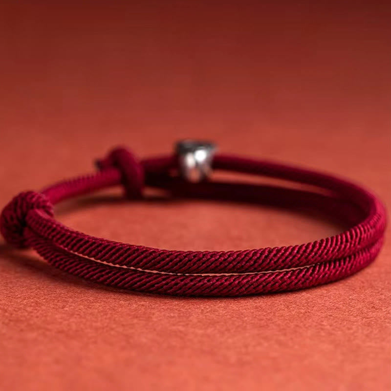 925 Silver Fu Character Braided Bracelet – Red twisted cord bracelet with silver fortune charm on red fabric background, flat lay diagonal overhead view