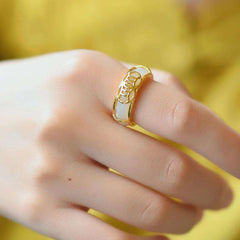 White Jade Luck Ring Necklace – Gold and white jade ring worn on finger showing geometric lattice inlay pattern with warm gold metalwork on soft yellow background
