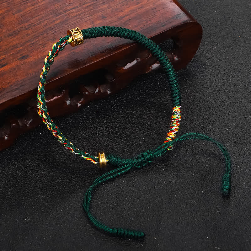 Om Mani Padme Hum Red String Bracelet – Deep green handmade bracelet with colorful braided sections and gold accents on black background with carved wood stand