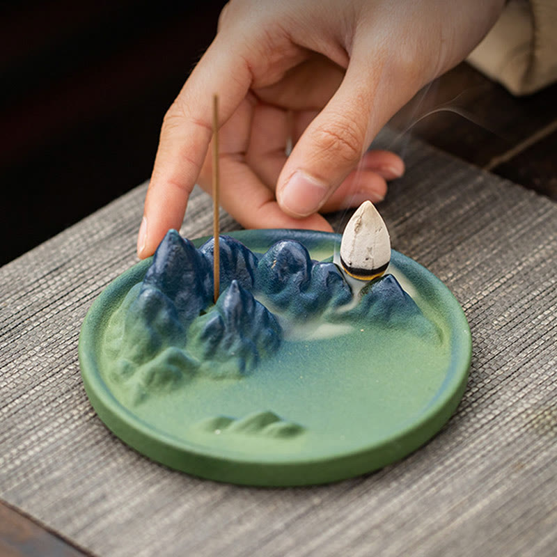 Ceramic Backflow Incense Burner – Hand holding blue mountain dish with dual incense and smoke, lifestyle zen shot