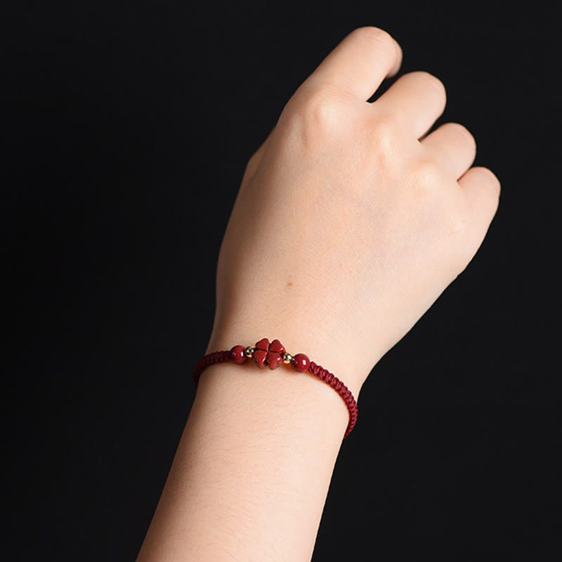 Burgundy braided cord bracelet with carved four-leaf clover charm and gold spacer beads worn on wrist against solid black background